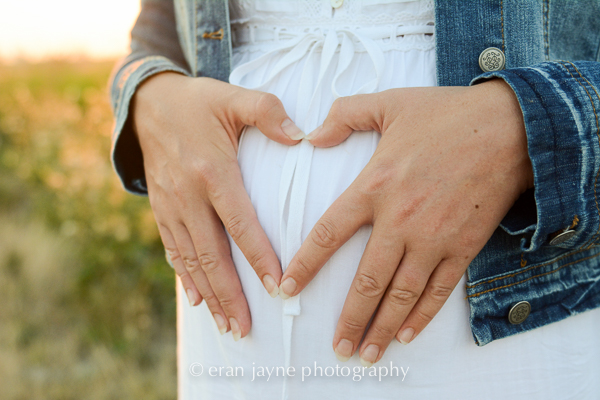 hands make heart on belly at sunset by eran jayne photography